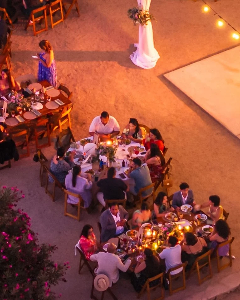 Guests seated at long candlelit tables at an outdoor group dinner